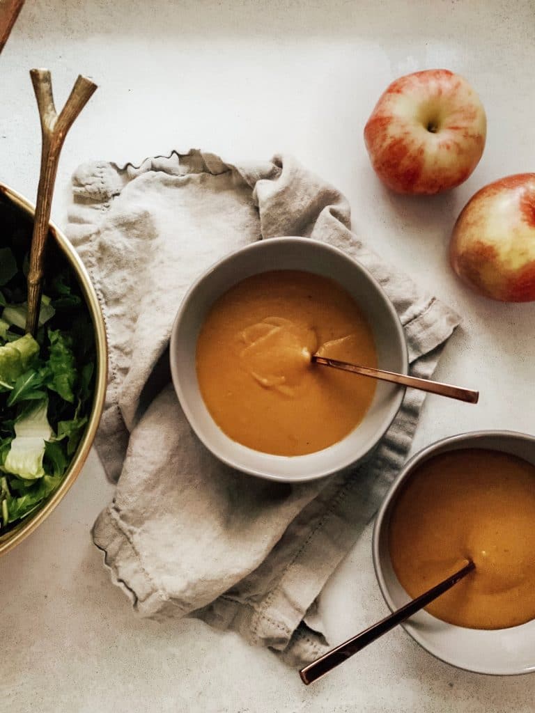Dairy-free roasted butternut squash soup served in bowls with fresh apples and greens on the side, perfect for a cozy, healthy meal.