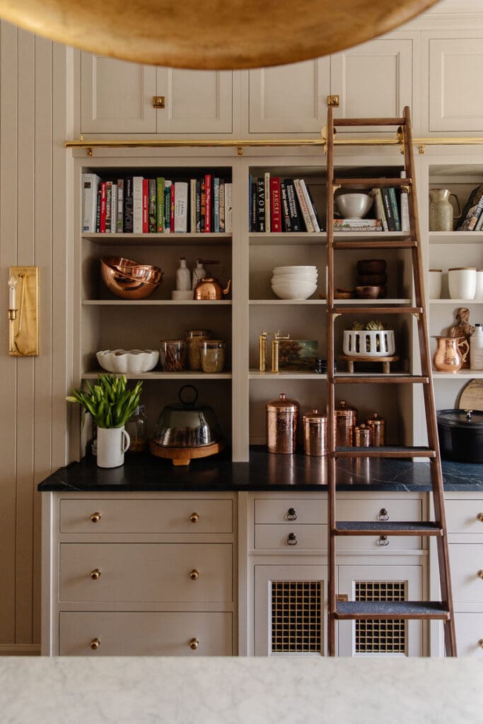 Stylish kitchen featuring open shelving, a wooden ladder, and a mix of white and copper accents, creating a warm and inviting space for cooking and entertaining.