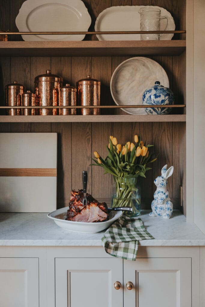 Caramelized Easter ham with carving fork in it and yellow tulips beside it.