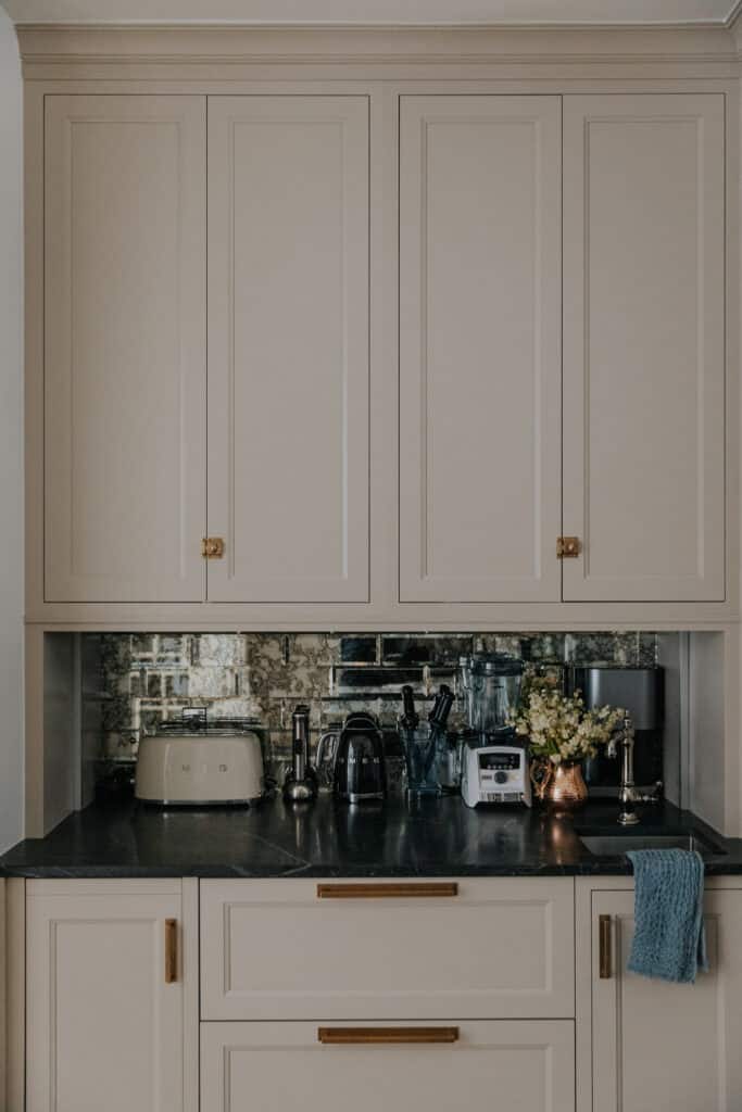 A kitchen counter with mirrored tile, a Smeg toaster, and a copper pot of flowers