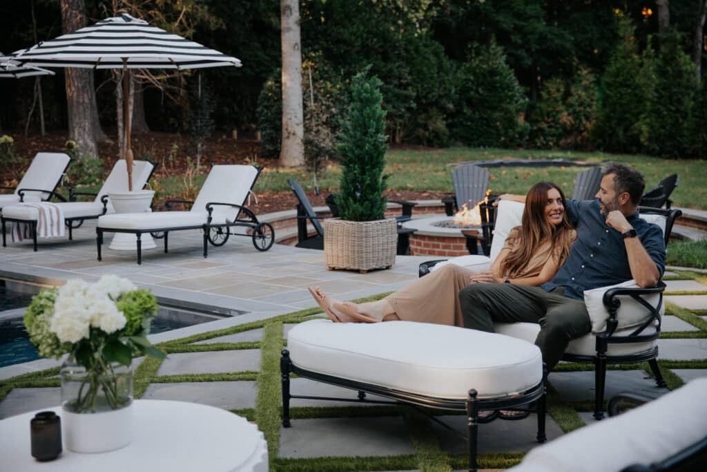 Relaxing couple enjoying outdoor furniture on a stylish backyard patio with lush greenery and modern seating.
