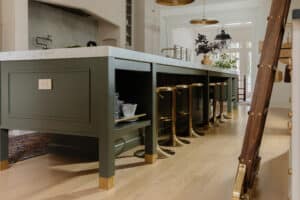 Modern kitchen island with a white marble countertop, green base, and gold accents, featuring bar stools in a contemporary home setting.