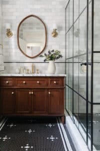 An elegant bathroom vanity featuring a dark wood cabinet, white marble countertop, and gold fixtures, complemented by a large mirror and a vase of fresh flowers.