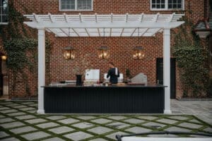 Modern outdoor kitchen featuring a black granite counter, pendant lights, and a brick wall backdrop with lush greenery for al fresco dining.