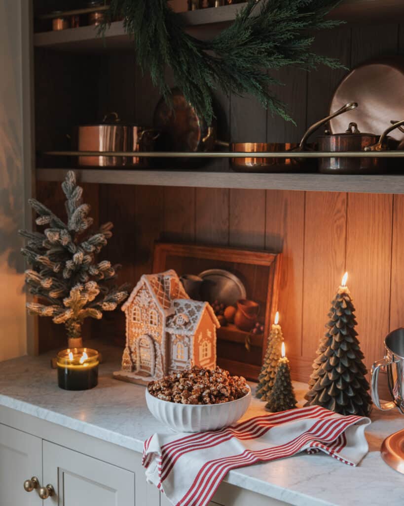 Chocolate Peppermint Caramel Corn in a scalloped bowl next to a gingerbread house and evergreen tree candles