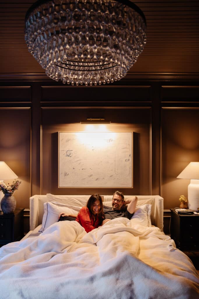 Julia and Chris cozied up in bed laughing with warm lamp lighting around them