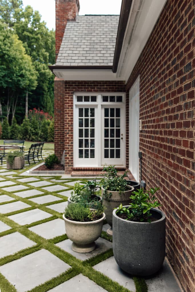 Outdoor herbs in large decorative pots placed along a brick house exterior, creating a lush, low-maintenance garden look outside.