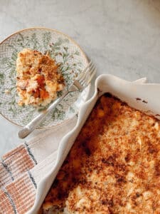 Cheeseless potato casserole in a white baking dish with a golden, crispy top, served alongside a slice on a decorative plate with a fork.