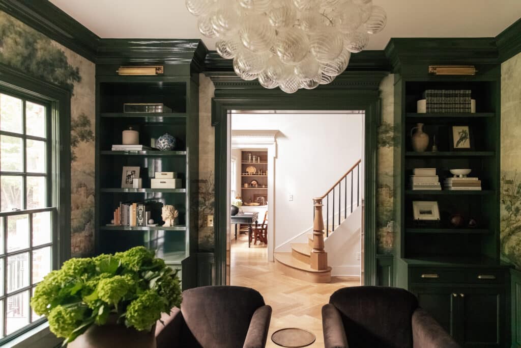 A stylish living room featuring dark green walls, built-in bookshelves filled with books and decor, and a large window allowing natural light to brighten the space.