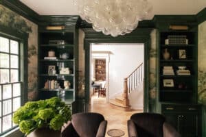 A stylish living room featuring dark green walls, built-in bookshelves filled with books and decor, and a large window allowing natural light to brighten the space.