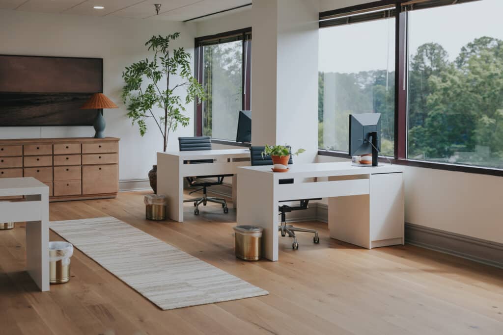 Two desks in a modern-looking office with large windows