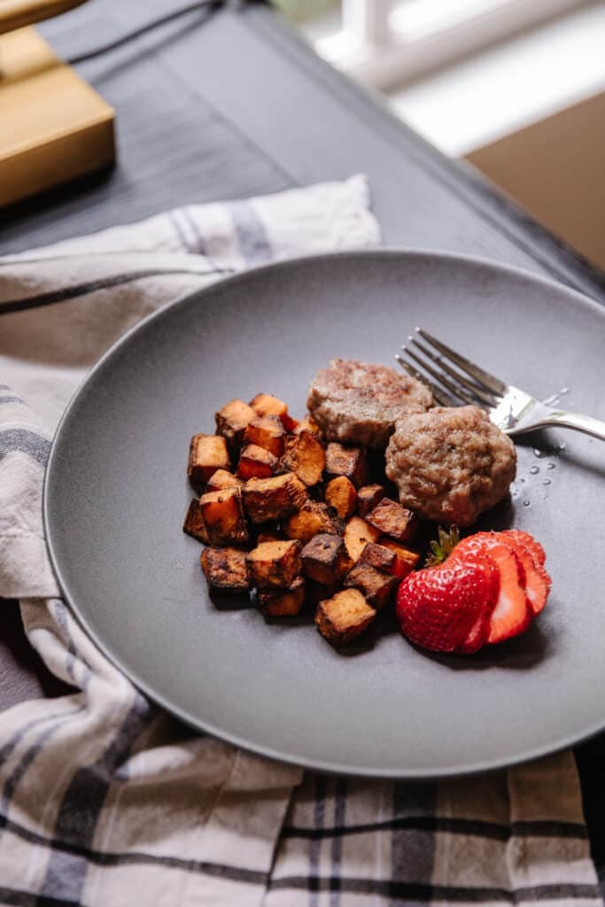 Sausage breakfast patties next to roasted sweet potatoes and a sliced strawberry on a gray plate