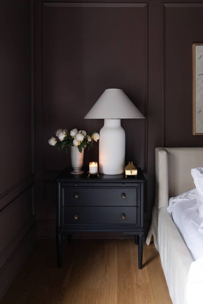 Chris Loves Julia | Candle on a gold footed candlestand on a nightstand in a bedroom