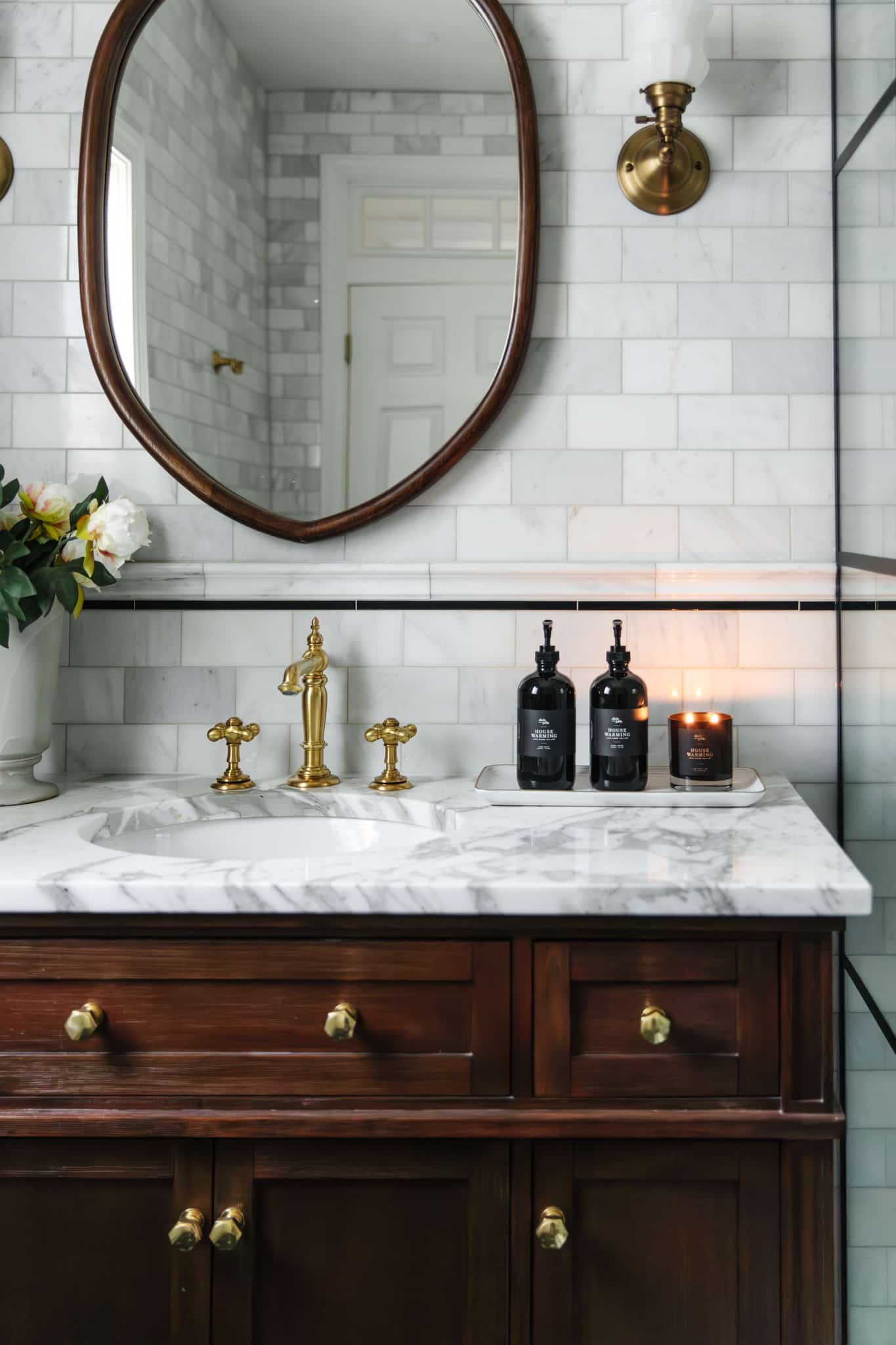 A sophisticated bathroom vanity featuring gold fixtures, marble countertop, and a large oval mirror, perfect for modern home decor.