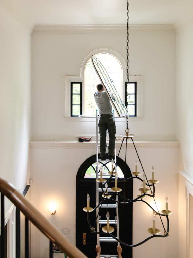 Man standing on a ladder in an entryway replacing an arched window