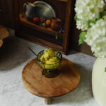 Dairy-free golden milk ice cream served in a glass bowl on a wooden stand, with a framed still life painting and white hydrangeas in the background, perfect for a healthy dessert.