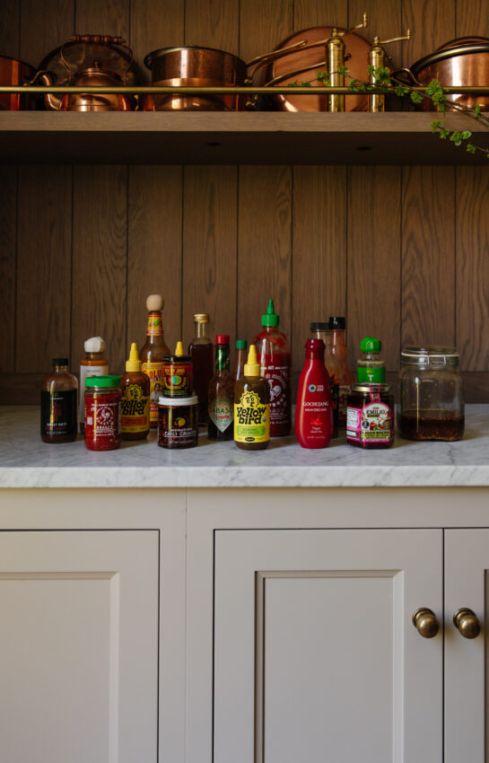 Assorted hot sauces displayed on a kitchen counter with wooden backsplash, showcasing popular brands for spicy food enthusiasts.