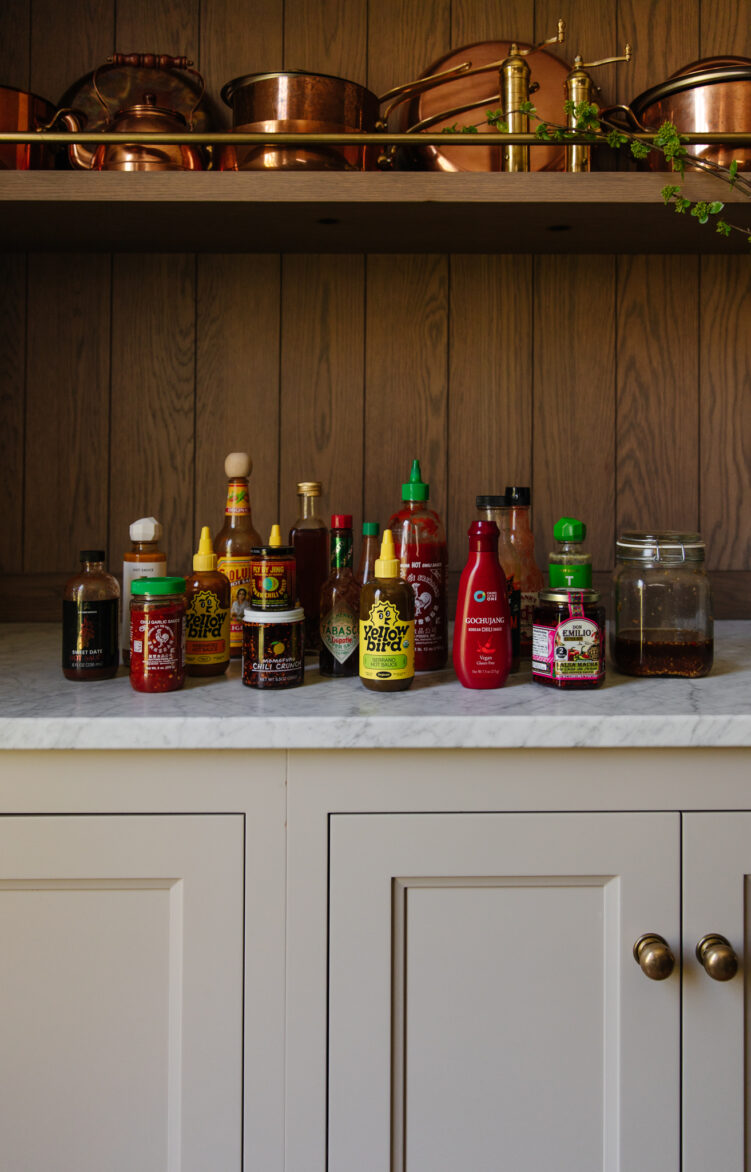 Assorted hot sauces displayed on a kitchen counter with wooden backsplash, showcasing popular brands for spicy food enthusiasts.