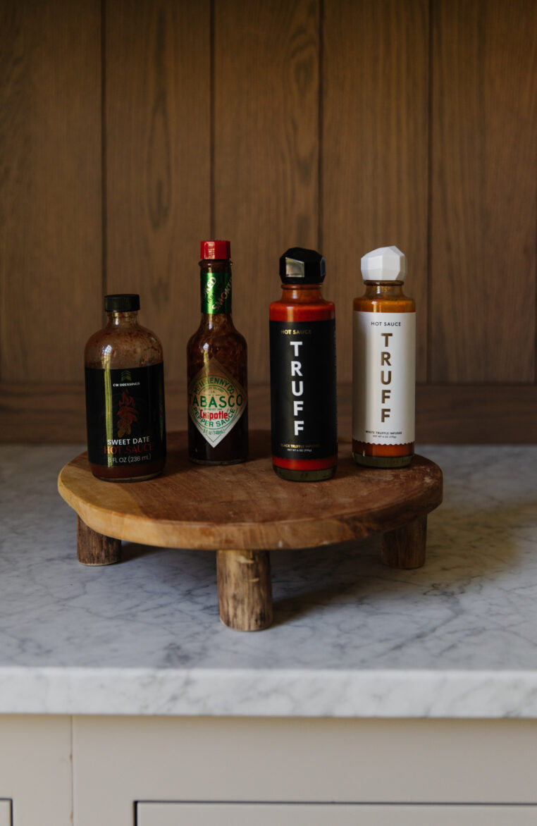 Chris' favorite hot sauces: Chipotle Tabasco Hot Sauce, Sweet Date Hot Sauce, Truff Hot Sauces displayed on a wooden serving board, showcasing popular spicy condiments for flavor enhancement.