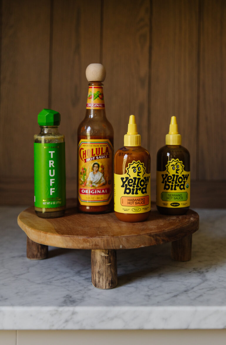 Assorted hot sauces including Truff, Cholula, and Yellowbird on a wooden serving board. Perfect for spicy food lovers