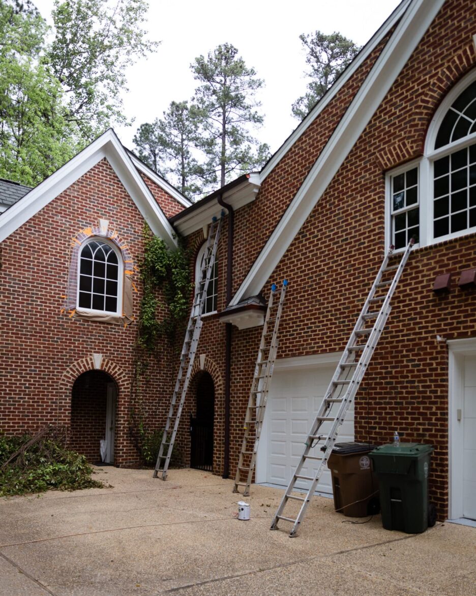 Exterior painting of window trim in progress with ladders