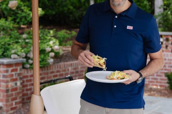 Man smiling while holding a plate of food at outdoor gathering.