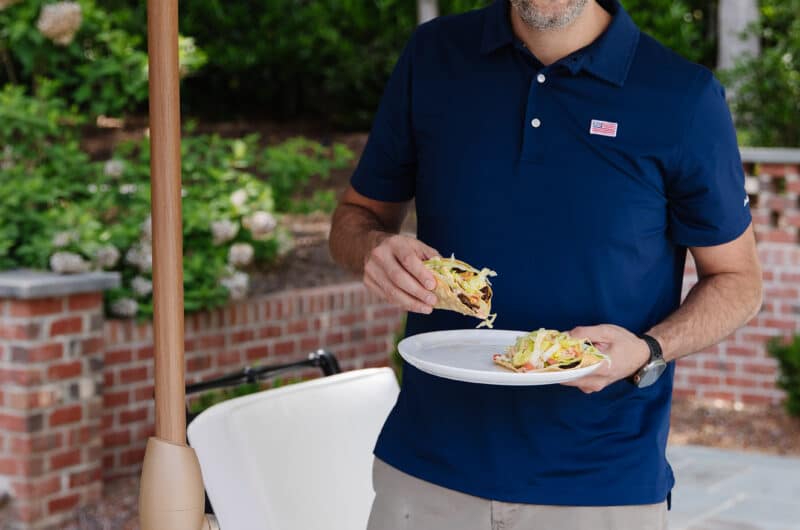 Man smiling while holding a plate of food at outdoor gathering.
