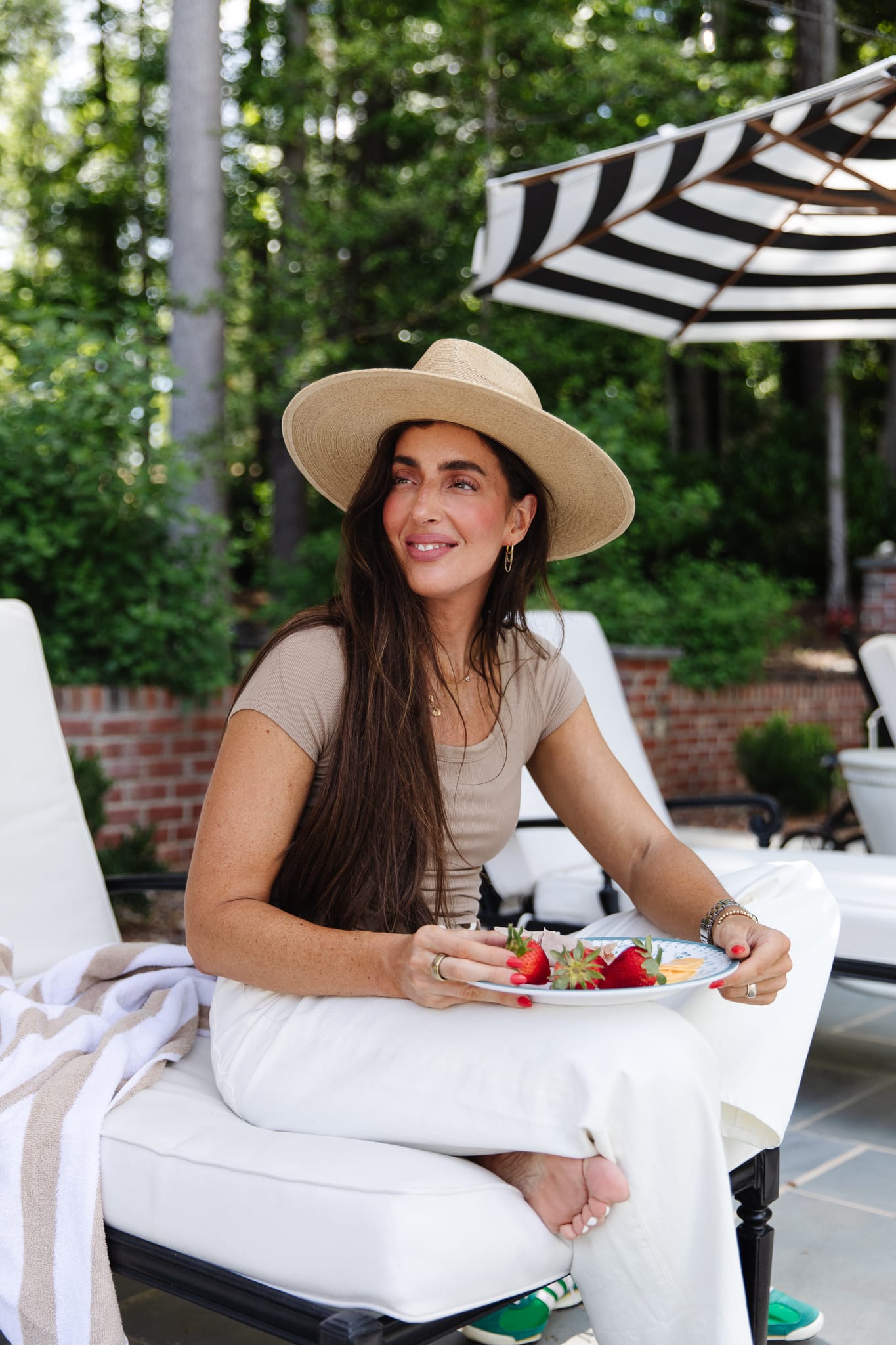 Julia sitting by the pool in a hat with a melamine plate of strawberries