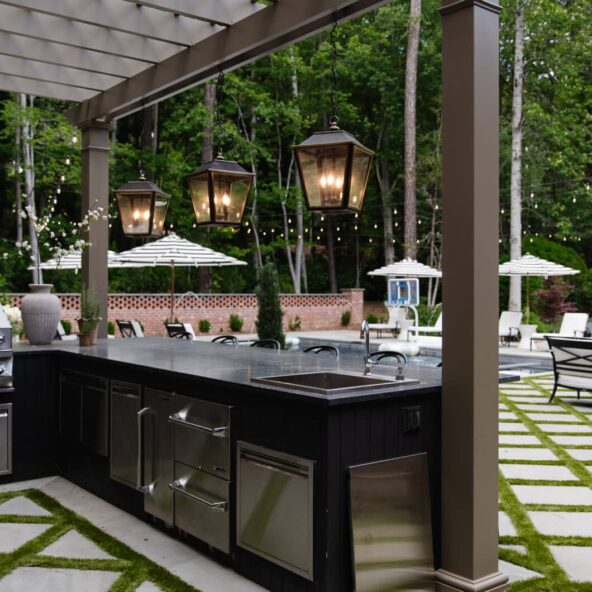 Charming outdoor bar area featuring hanging lanterns, string lights, and a sleek black countertop, perfect for outdoor gatherings and summer evenings.