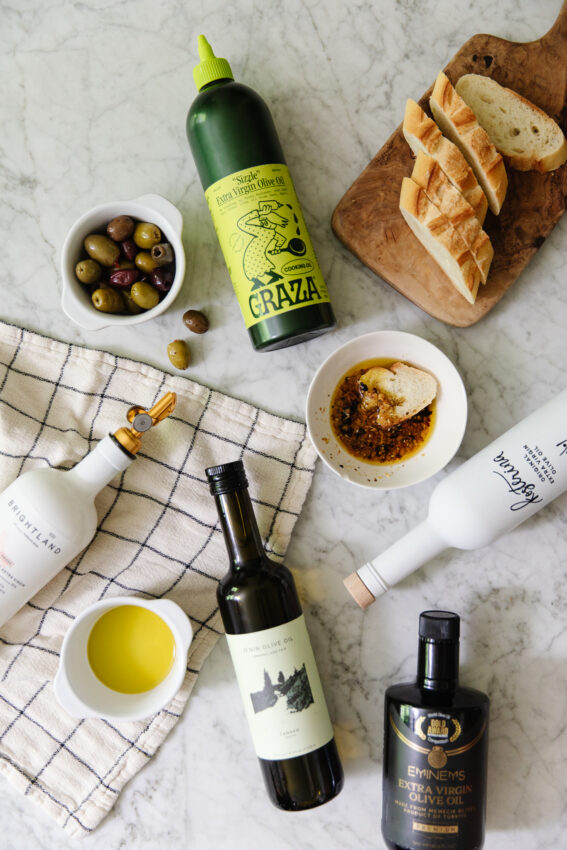 High-quality extra virgin olive oil with fresh bread and olives on a marble surface.
