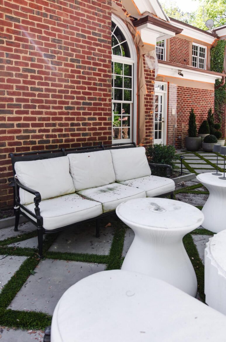 Outdoor furniture with leaves and mildew before cleaning set against a classic red brick house with large arched windows and lush greenery.