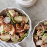 Delicious potato salad featuring radishes, asparagus, and a creamy dressing, served in white bowls on a marble surface. Perfect for summer gatherings or casual meals.
