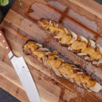 Delicious grilled pork tenderloin topped with creamy macadamia nut pesto, served on a wooden cutting board.