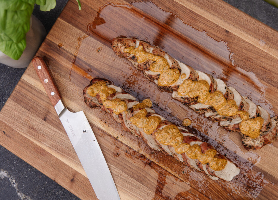 Delicious grilled pork tenderloin topped with creamy macadamia nut pesto, served on a wooden cutting board.