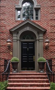 Beautiful brick home with a classic black front door, flanked by two lantern-style lights and potted plants, showcasing a welcoming entryway perfect for painting projects.