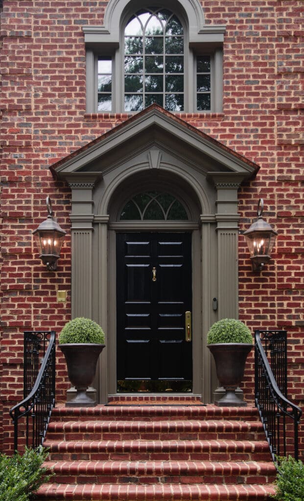 Beautiful brick home with a classic black front door, flanked by two lantern-style lights and potted plants, showcasing a welcoming entryway perfect for painting projects.