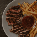 A sliced steak next to fries and a dipping sauce