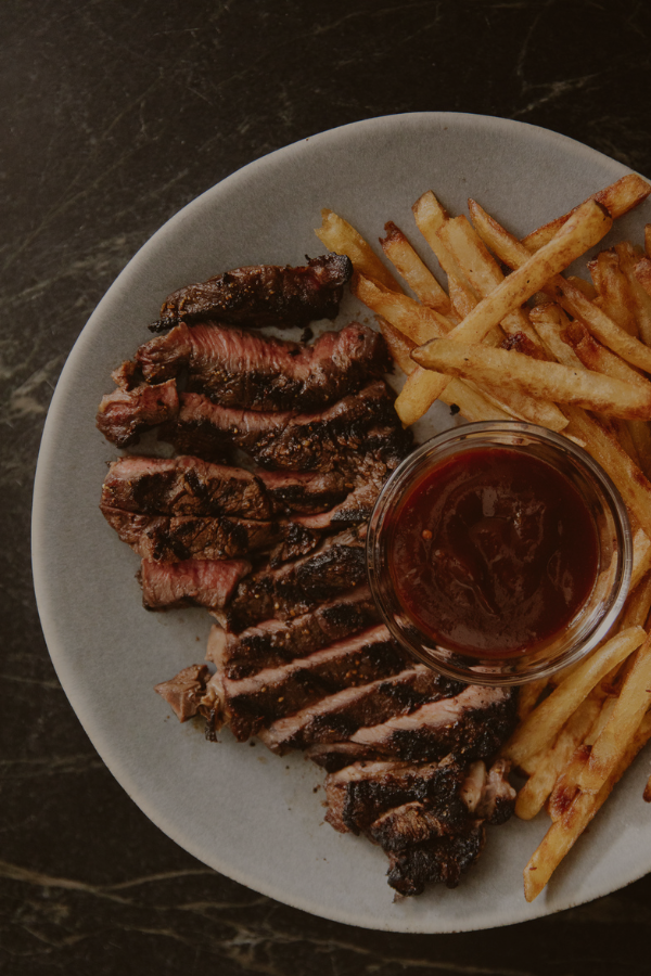 A sliced steak next to fries and a dipping sauce