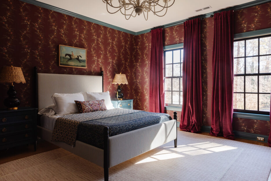 Elegant bedroom featuring red patterned wallpaper, large windows with red curtains, and a cozy bed with decorative pillows, creating a warm and inviting atmosphere.