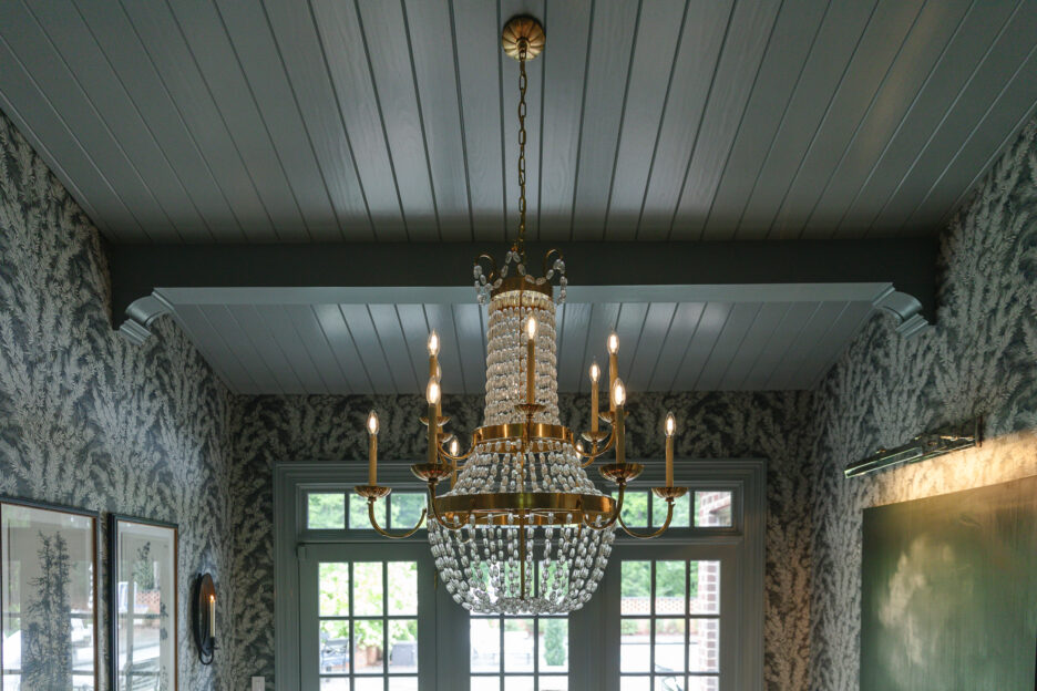 A dining room with ceiling beams, planks, and corbels painted smokey gray-blue
