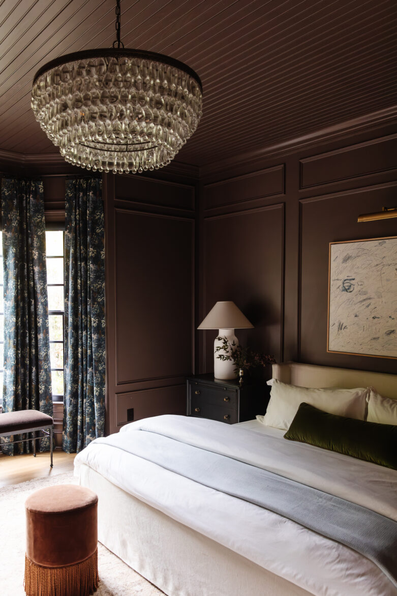 Luxurious bedroom with dark paneled walls, elegant chandelier, and cozy decor, showcasing stylish interior design ideas from Chris Loves Julia.