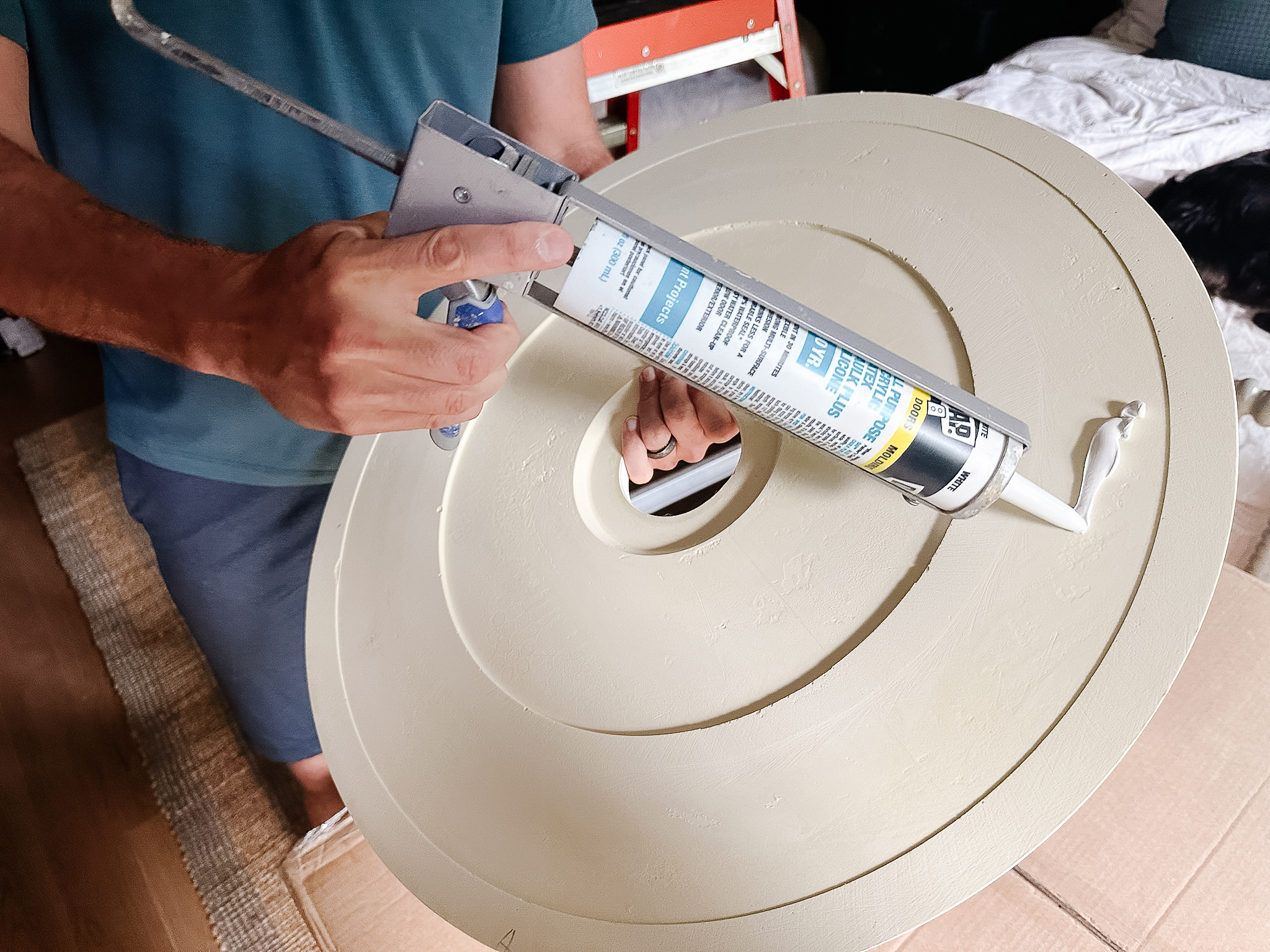 Chris Loves Julia | Chris applying liquid nail compound to the back of a white ceiling medallion in Greta's room