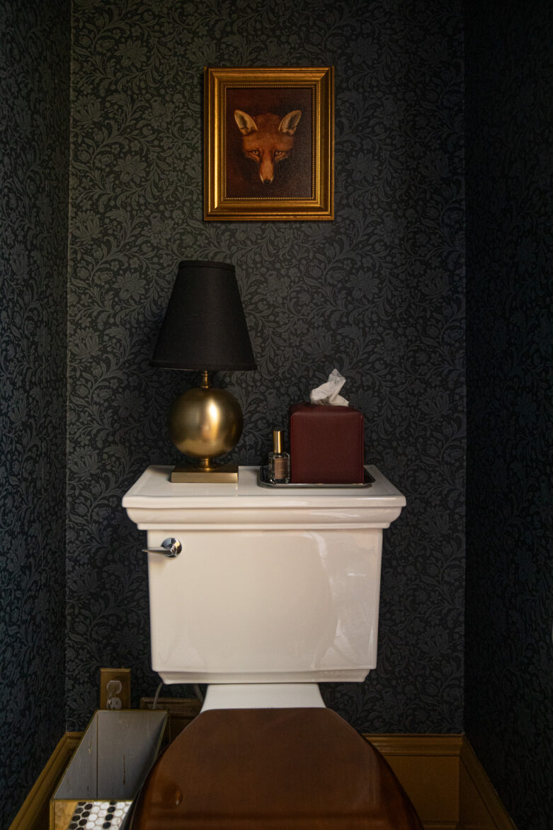 Dark floral wallpaper, framed fox art, black lamp, gold decor, tissue box, bathroom interior, home decor inspiration.