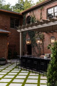 Charming outdoor dining space featuring a brick house, pergola, and stylish black chairs, perfect for entertaining in a cozy backyard setting.