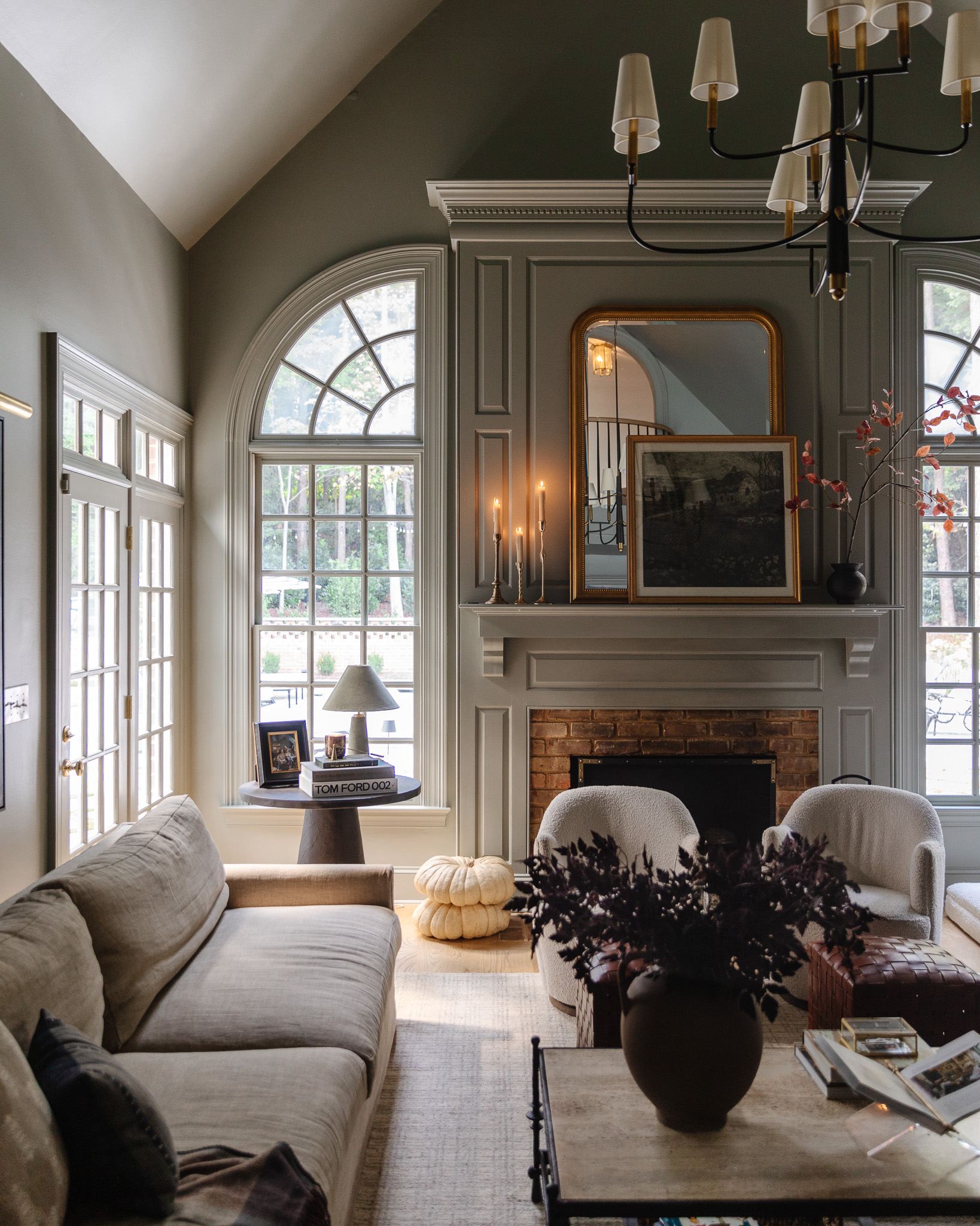 Chris Loves Julia | Living room with white pumpkins by the hearth and burgundy faux stems in a vase on the coffee table