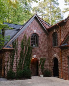 Beautiful brick house featuring arched windows and ivy climbing the exterior walls, surrounded by lush trees in a serene residential setting.