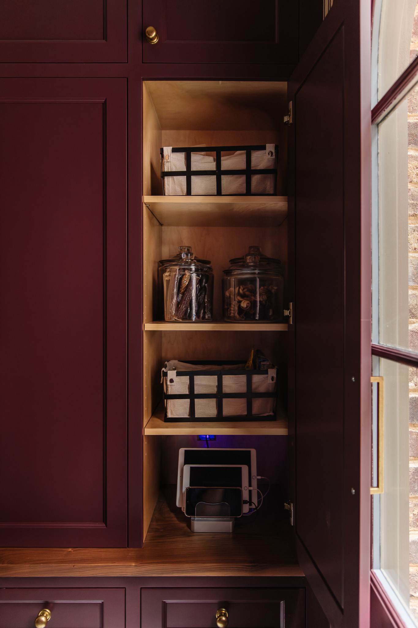 Chris Loves Julia | Moody dark red mudroom with a locker door open to show a charging station for iPads and a few canvas-lined baskets