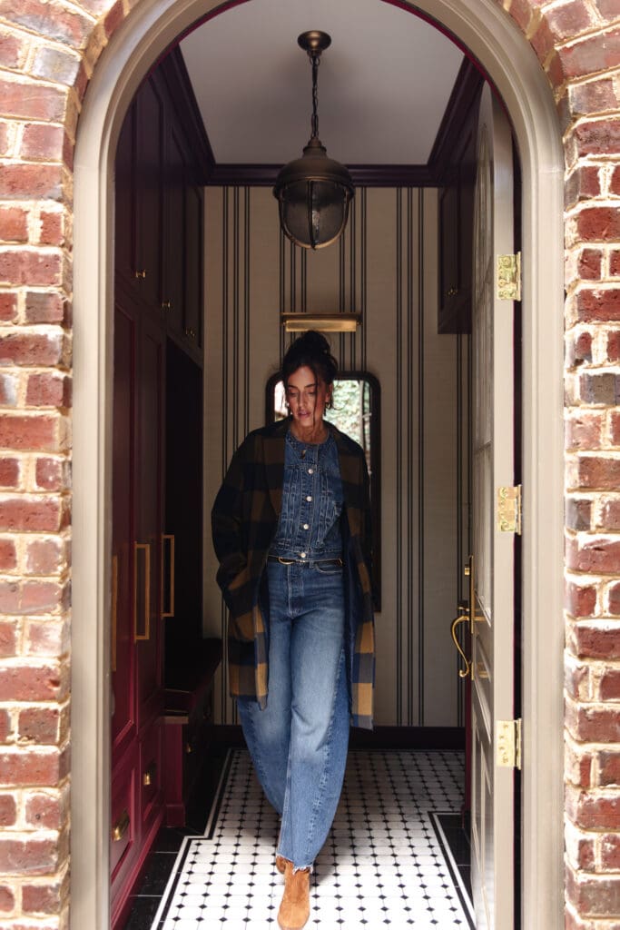 Julia walking out of the mudroom in denim barrel jeans, a denim top and jacket