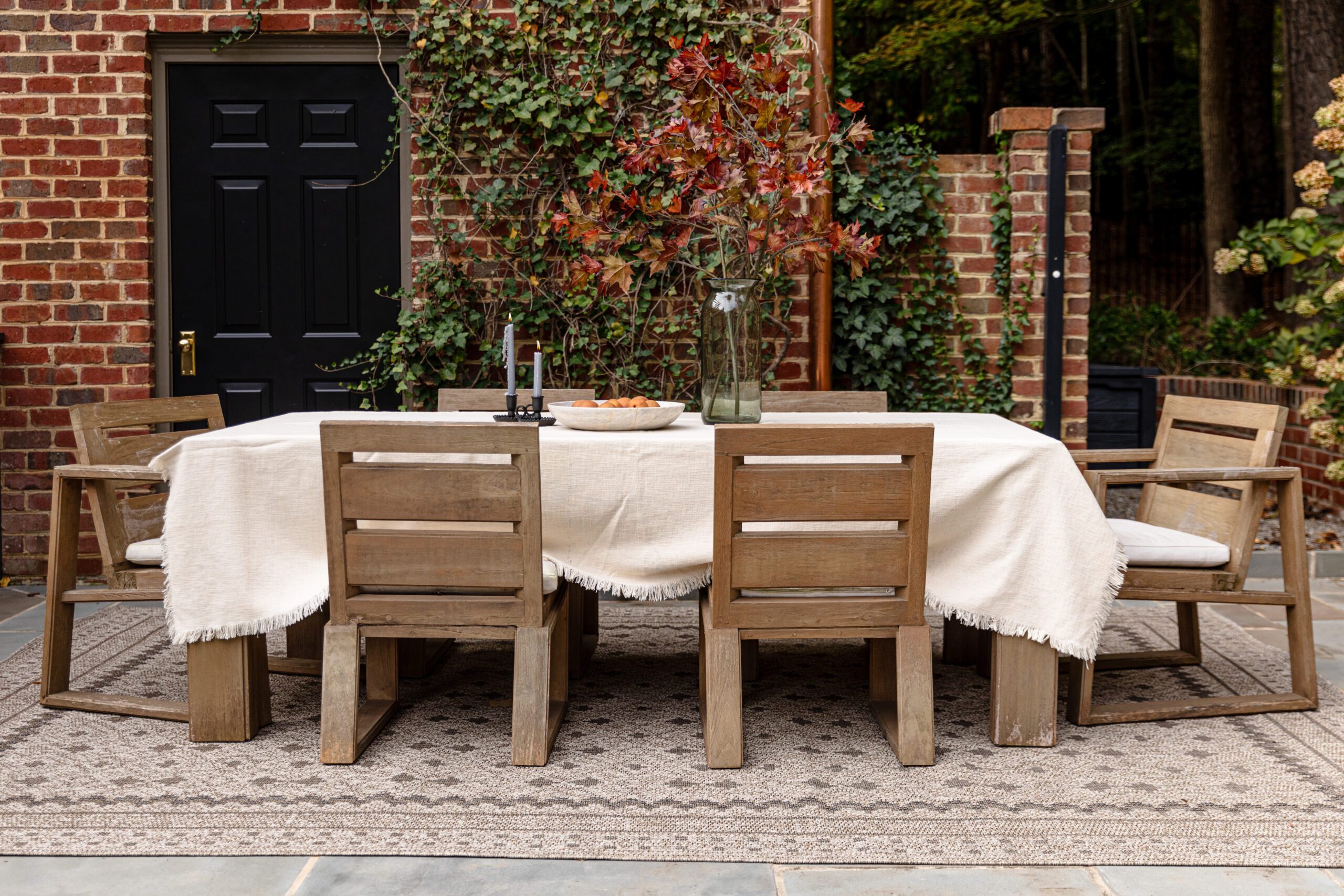 Outdoor dining table scene in front of ivy brick wall with a beautiful beige geometric outdoor rug