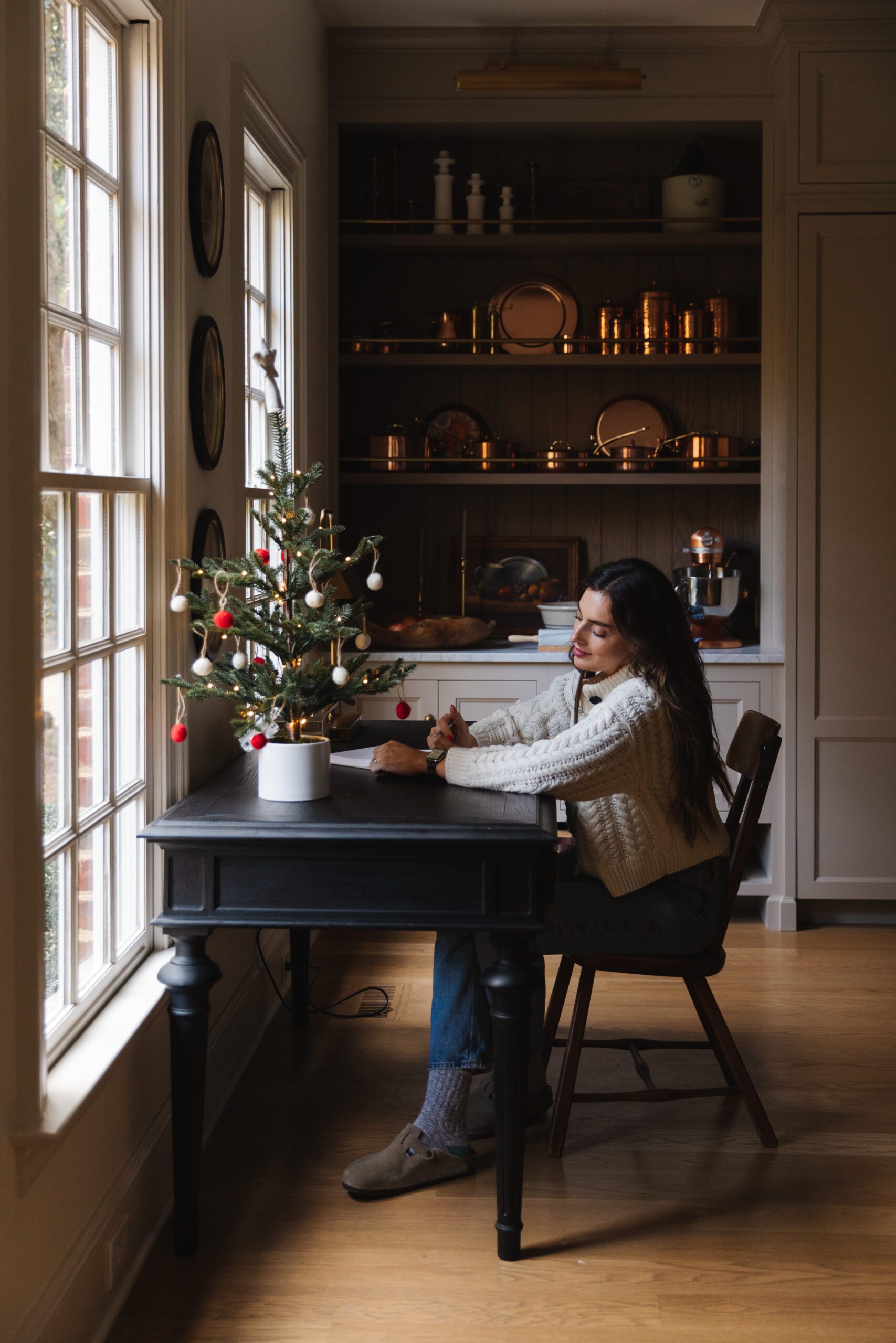 Julia at the kitchen writing desk with a tabletop Christmas tree adorned with bobble ornaments